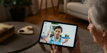 Een oudere vrouw in een videogesprek met een fysiotherapeut op een tablet, een voorbeeld van AI in de zorg die comfort en moderne zorgtechnologie benadrukt.