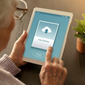 Handen van een oudere persoon houden een tablet vast met een duidelijk cloud-back-upscherm voor foto’s, gericht op veilige opslag en digitale vaardigheden voor ouderen