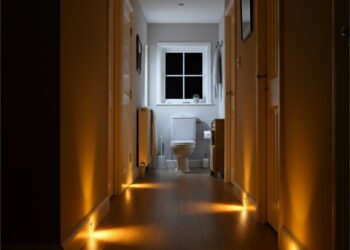 Nachtelijke hal met warme bewegingssensor-lampjes langs de plint die een veilig pad naar de badkamer verlichten; helpt struikelgevaar verminderen zonder kabels of obstakels