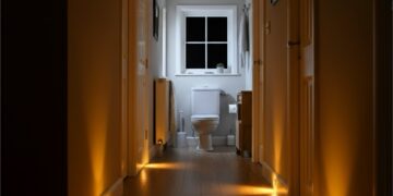 Nachtelijke hal met warme bewegingssensor-lampjes langs de plint die een veilig pad naar de badkamer verlichten; helpt struikelgevaar verminderen zonder kabels of obstakels