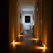 Nachtelijke hal met warme bewegingssensor-lampjes langs de plint die een veilig pad naar de badkamer verlichten; helpt struikelgevaar verminderen zonder kabels of obstakels